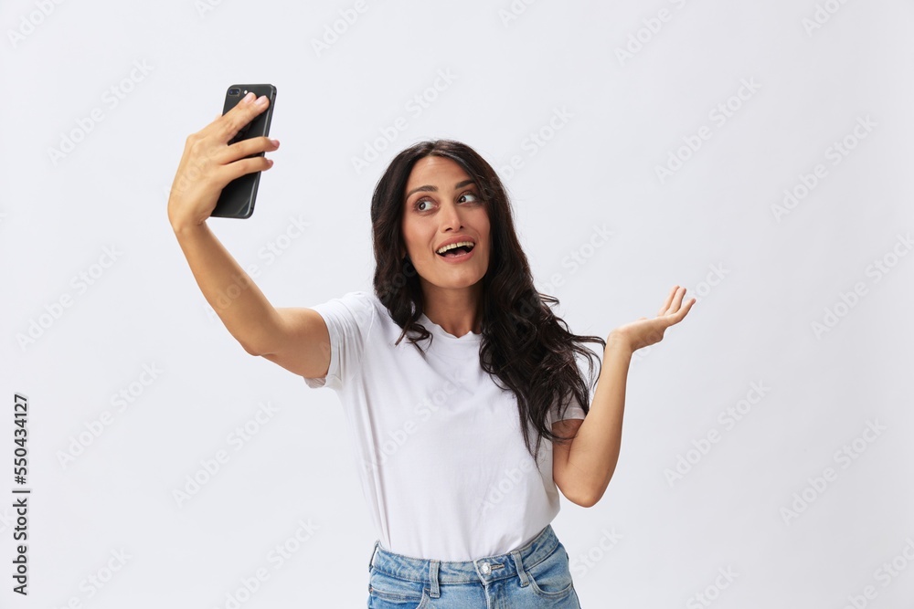 Woman blogger with a phone in her hands photo content, video call, selfie smile with teeth in a white t-shirt on a white background, copy space, emotions and gestures signals Woman blogger with a phone in her hands photo content, video call, selfie smile with teeth in a white t-shirt on a white background, copy space, emotions and gestures signals