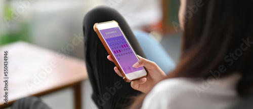 Mobile application for monitoring the menstrual cycle on the smartphone screen in the hands of the woman. The woman is sitting on the sofa with the mobile.