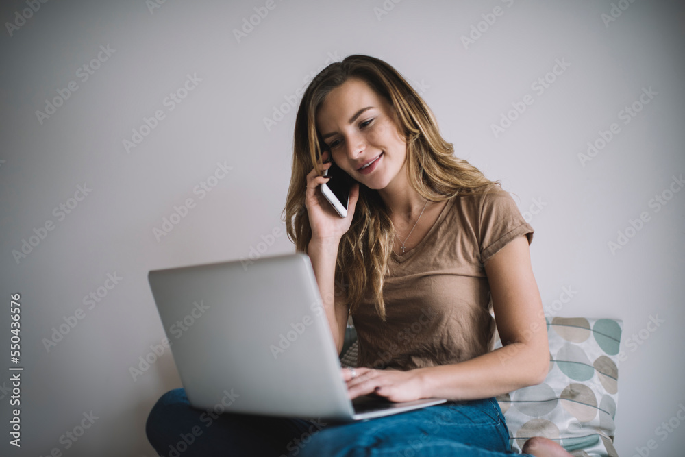 Caucasian hipster girl calling to friend for invite to evening movies searching video on popular website, millennial female freelancer checking laptop update during smartphone conversation via app Caucasian hipster girl calling to friend for invite to evening movies searching video on popular website, millennial female freelancer checking laptop update during smartphone conversation via app