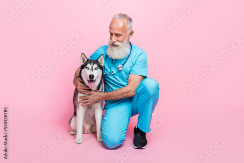 Full size photo of professional specialist pensioner doctor wear blue uniform sitting cuddle husky isolated on pink color background © deagreez