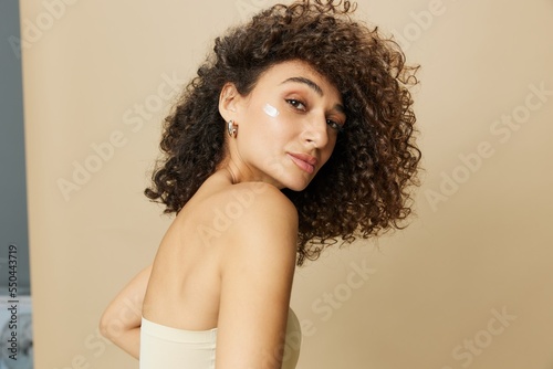 Woman beauty face close-up applying anti-aging moisturizer with fingers of her hand, skin health nails and hair, hair dryer style curly afro hair, body and beauty care concept