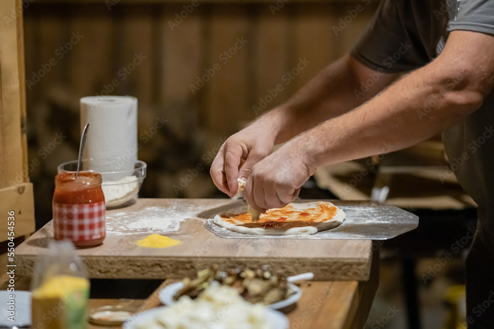 Man preparing a delicious fresh home made pizza. Person topping pizza dough with mushrooms, tomatoes, cheese and so on.