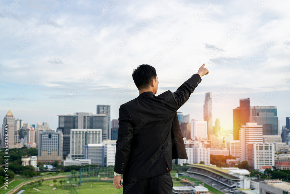 businessman standing on tall building behind cityscape is pointing at goal achievement target with business success concept businessman standing on tall building behind cityscape is pointing at goal achievement target with business success concept