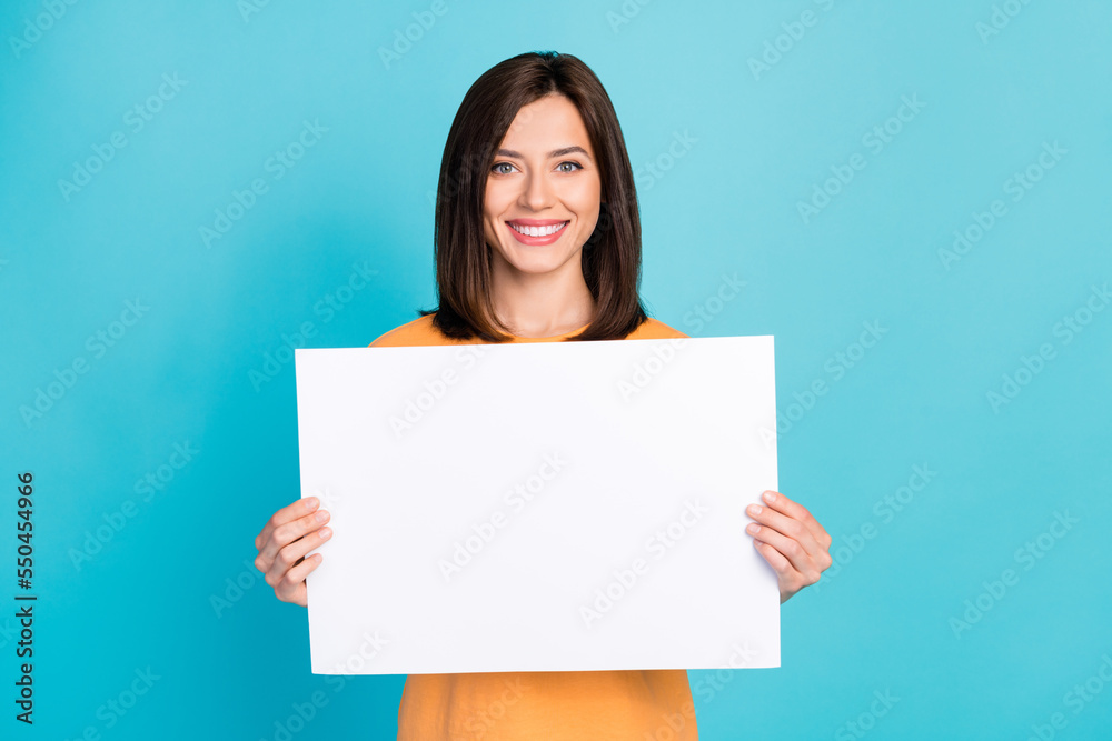 Portrait of good mood adorable pretty woman with long hairstyle wear yellow t-shirt hold white poster isolated on blue color background Portrait of good mood adorable pretty woman with long hairstyle wear yellow t-shirt hold white poster isolated on blue color background