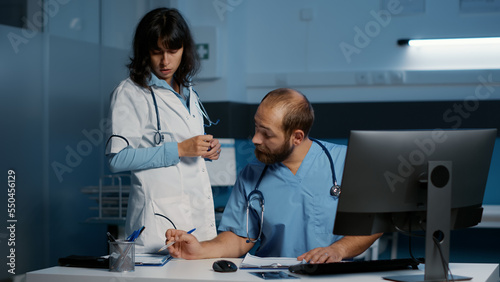 Medical team analyzing patient disease report on computer while working over hours in hospital office. Doctor and assistant planning health care treatment to help cure illness. Medicine service