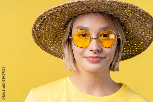 Portrait of young pretty blonde woman on summer yellow studio background. Confident sunny outfit with sunglasses and straw hat.