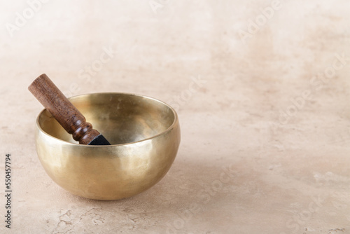 Tibetan singing bowl with stick used during mantra meditations on beige stone background, copy space. Sound healing music instruments for meditation, relaxation, yoga, massage, mental health