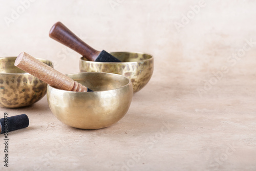 Tibetan singing bowls with sticks used during mantra meditations on beige stone background, copy space. Sound healing music instruments for meditation, relaxation, yoga, massage, mental health