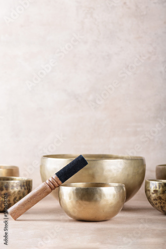 Tibetan singing bowls with sticks used during mantra meditations on beige stone background, copy space. Sound healing music instruments for meditation, relaxation, yoga, massage, mental health