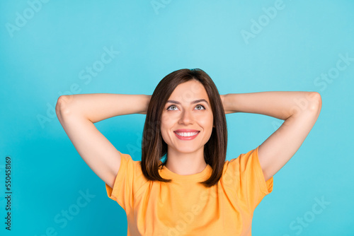 Portrait of optimistic satisfied woman long hairstyle yellow t-shirt look empty space hands behind head isolated on blue color background © deagreez