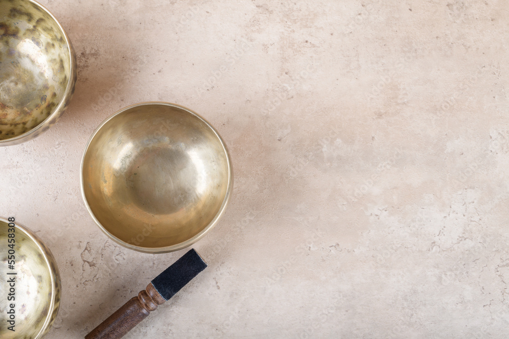 Tibetan singing bowls with stick used during mantra meditations on beige stone background, top view, flat lay. Sound healing music instruments for meditation, relaxation, yoga, massage, mental health