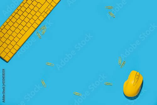 Yellow keyboard, wireless computer mouse, paperclips on a blue background. Top view, flat lay