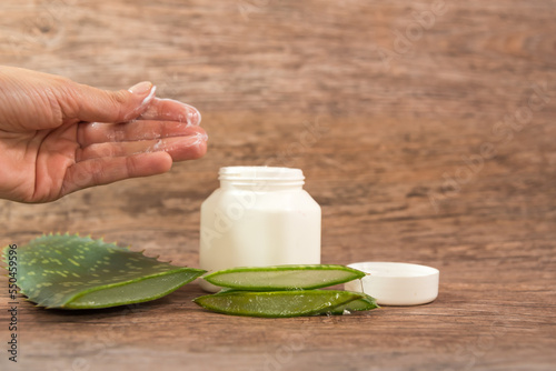 hand with moisturizer next to pieces of Aloe Vera and a plastic container