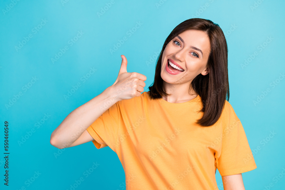 Portrait of glad pleasant cute woman with long hairstyle dressed yellow t-shirt showing thumb up isolated on blue color background Portrait of glad pleasant cute woman with long hairstyle dressed yellow t-shirt showing thumb up isolated on blue color background