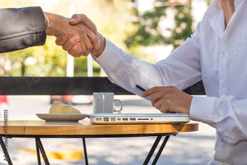 Two people shaking hands sitting outside a cafe