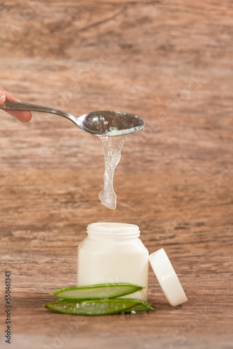 person placing Aloe Vera pulp in a plastic container with a metal spoon