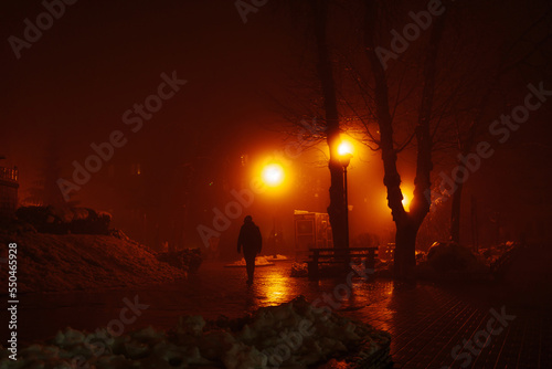 Silhouette of a man walking in the night park in the fog. Dramatic red light from lanterns. The effect of soft focus, sleep. The effect of soft focus, sleep.