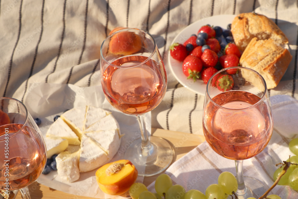 Glasses of delicious rose wine and food on white picnic blanket Glasses of delicious rose wine and food on white picnic blanket
