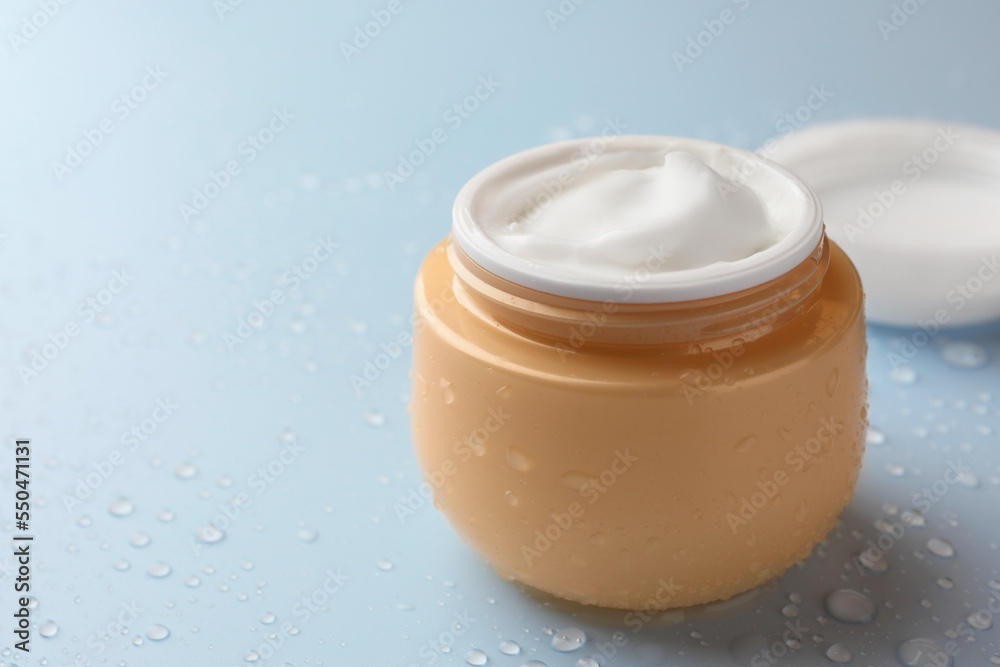 Jar of face cream on light blue surface covered with water drops, space for text Jar of face cream on light blue surface covered with water drops, space for text