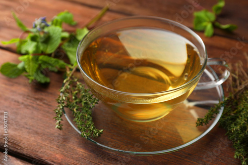 Cup of aromatic herbal tea and fresh thyme on wooden table, closeup