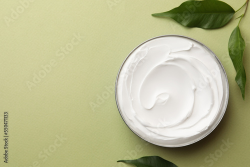 Jar of face cream and fresh leaves on light green background, flat lay. Space for text