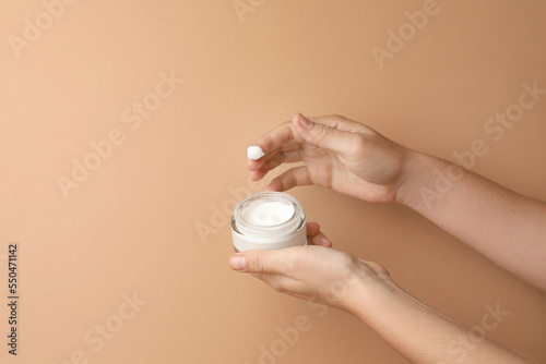 Woman applying face cream on beige background, closeup. Space for text