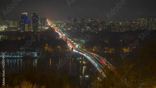 Kyiv, Ukraine dusk time-lapse. Aerial view of railway bridge, left bank of Kyiv and Brovarsky Avenue across the Dnipro River. Light trails from the car and subwa run along the bridge and the avenue. photo