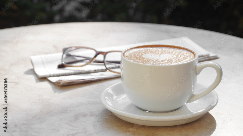 Cup of delicious coffee, glasses and newspaper on beige marble table outdoors, space for text Cup of delicious coffee, glasses and newspaper on beige marble table outdoors, space for text
