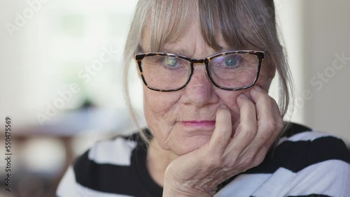 Close up of senior white woman at home looking at camera with her chin resting on her hand. Older Caucasian lady with grey hair in striped sweater in her living room. Slow motion handheld 4k photo