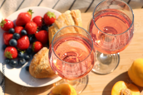 Glasses of delicious rose wine and food on wooden board, closeup