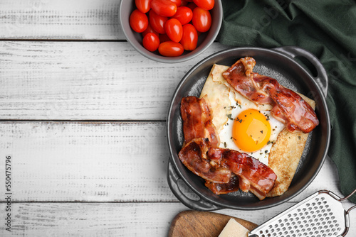 Quadro em tela Delicious crepe with egg and bacon in dish on white wooden table, flat lay with space for text