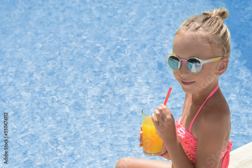 Cute little girl with glass of juice near swimming pool on sunny day. Space for text