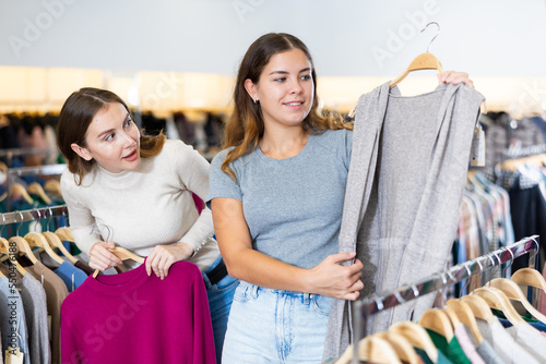 Two cheerful female friends comparing raspberry jumper and gray buttonless cardigan in a clothing store photo