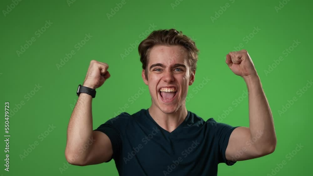 Excited jubilant overjoyed young man 20s doing winner gesture celebrate clenching fists say yes isolated on green screen background studio portrait in slow motion