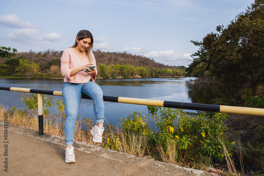 Fototapeta premium young woman with cell phone by the lake