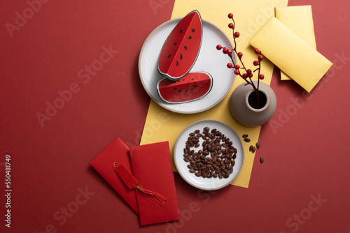 Asia Holiday in Spring. Red background arranged—accessories watermelon crafts, watermelon seeds, a vase of flowers,s and yellow envelopes.