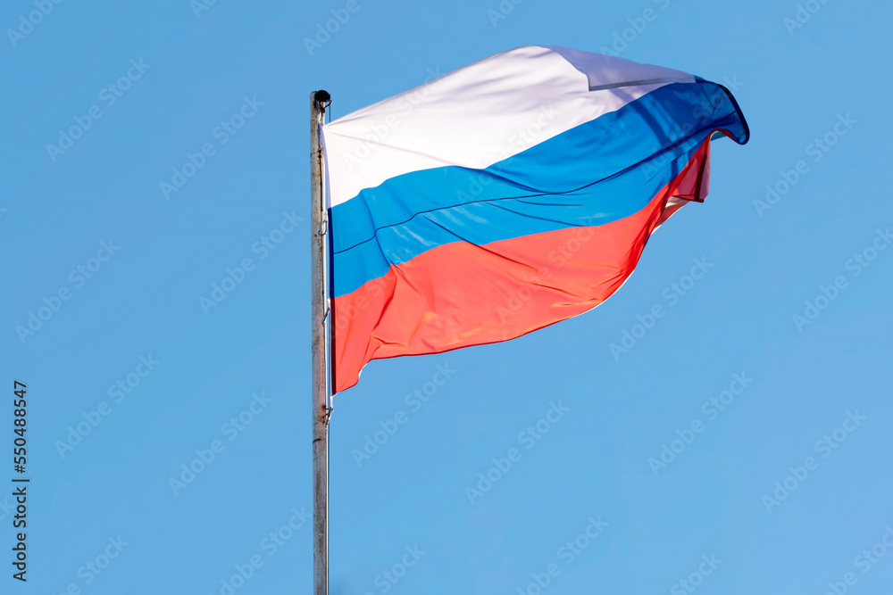 The flag of Russia on the flagpole flutters against the blue sky The flag of Russia on the flagpole flutters against the blue sky