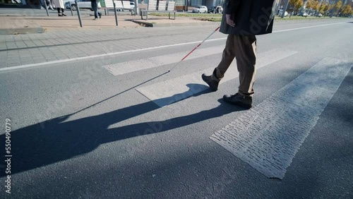 Visually impaired man crossing the road with his stick with the help of tactile pedestrian sidewalk for the visually impaired in the city.