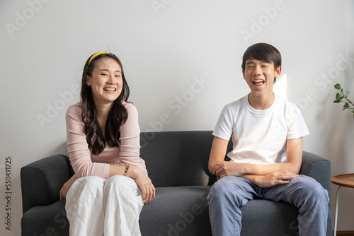 Asian brother and sister hugging with care and love sit on sofa at home.