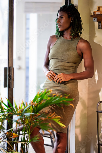 Black woman with green dreadlocks  wearing green dress standing in patio entrance