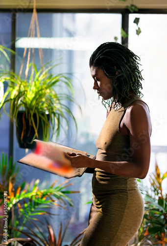 Black woman with green dreadlocks  wearing green dress standing in the living room, reading book