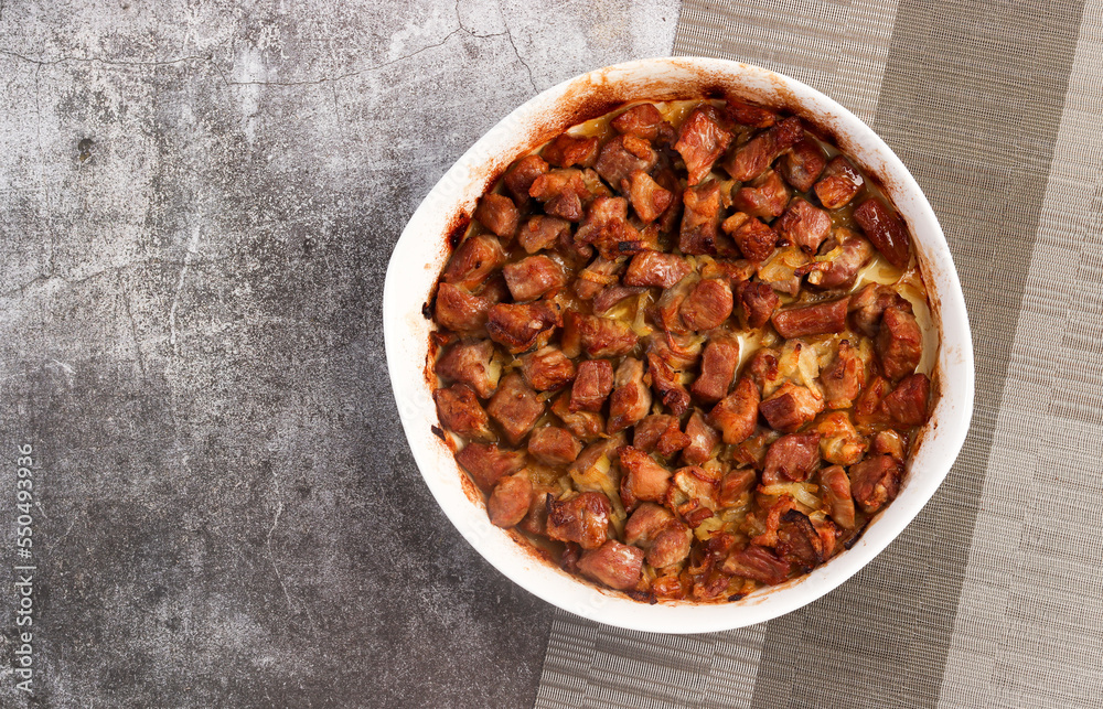 Roasted pork meat with onions in a white baking dish on a dark grey background. Top view, flat lay Roasted pork meat with onions in a white baking dish on a dark grey background. Top view, flat lay
