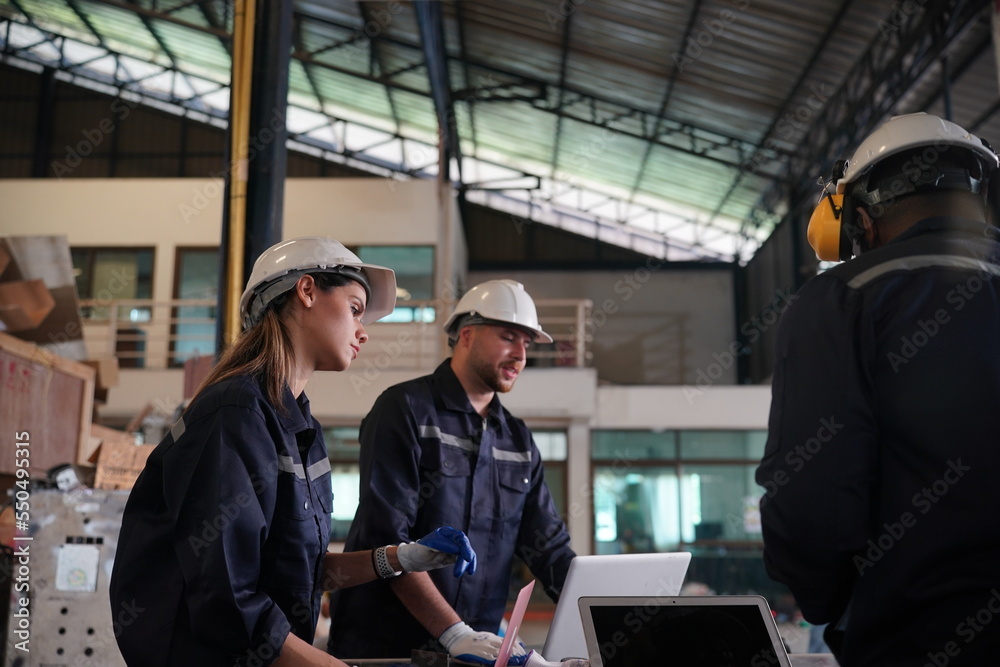 Young successful technician or repairman of industrial machines in safety helmet and workwear standing in large garage or workshop Young successful technician or repairman of industrial machines in safety helmet and workwear standing in large garage or workshop