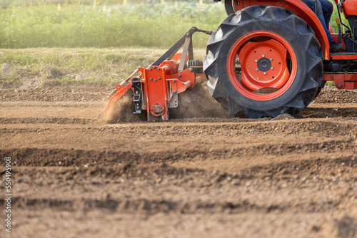 Tractor cultivating land with a rotary tiller in farm.