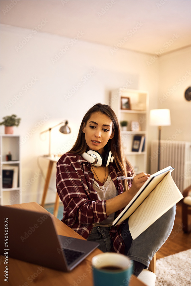 Female student using computer while learning and writing notes at home. Female student using computer while learning and writing notes at home.