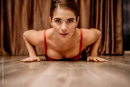 Young woman in red corset and black leather pants. Sexy seductive brunette  fitness instructor doing stretching and pilates on yoga mat at home. Female fitness yoga concept. Role play. Entertainment.