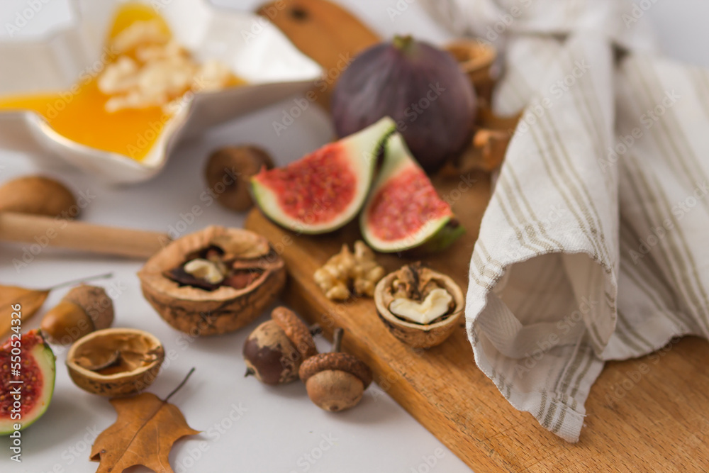 Autumn still-life with ripe figs cut in slices, walnuts and plate full of honey on wooden cutting board. Healthy snacks.