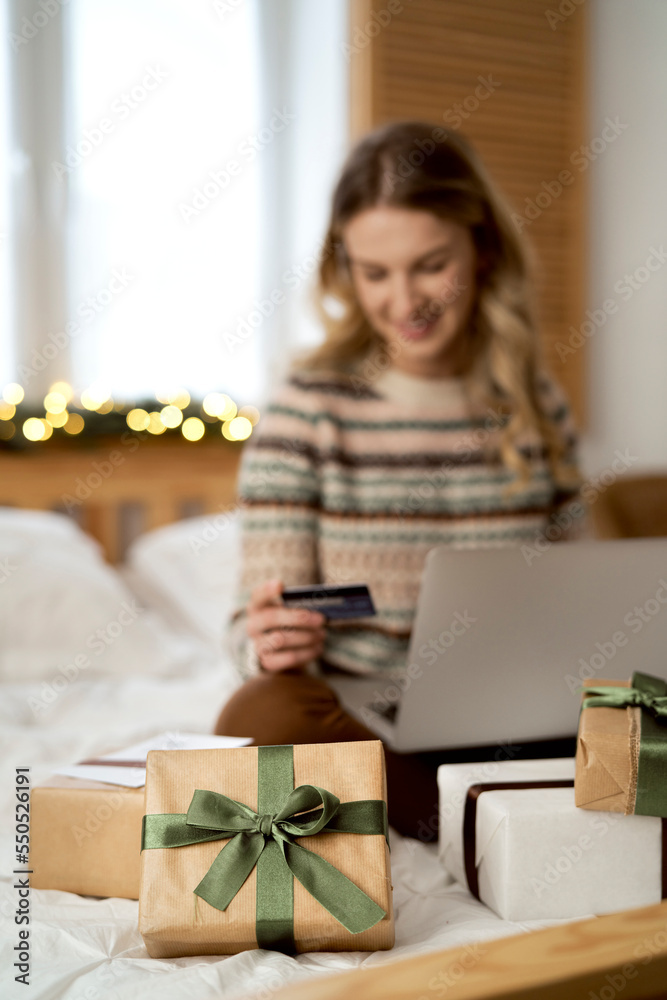 Caucasian woman sitting on bed and doing Christmas shopping with use of laptop and credit card Caucasian woman sitting on bed and doing Christmas shopping with use of laptop and credit card