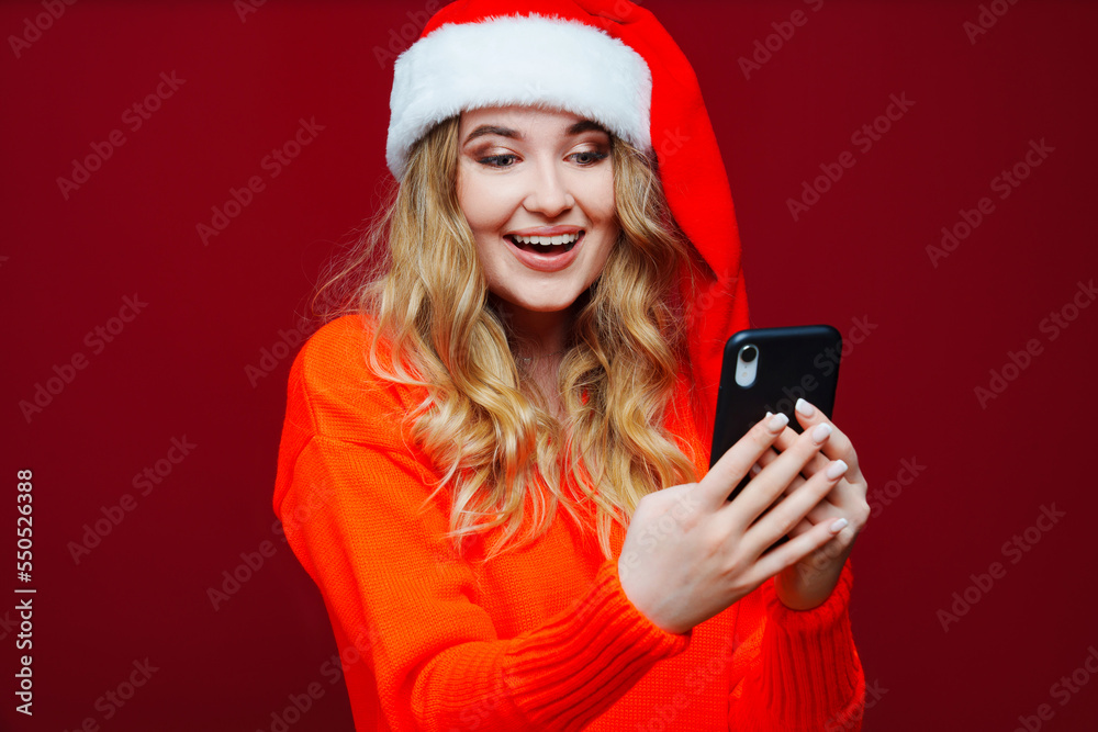 a beautiful woman in a Santa Claus hat with smartphone on a red background. a beautiful woman in a Santa Claus hat with smartphone on a red background.