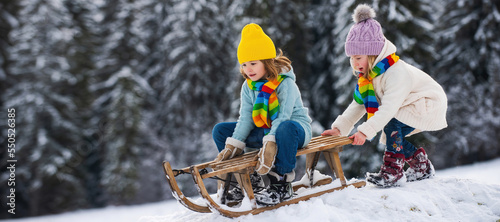Cute girl and boy enjoying a sleigh ride. Children sledding in snow on winter park.